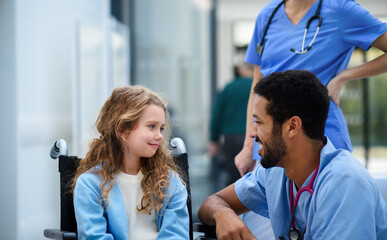 Young multiracial doctor talking with little girl on wheelchair.