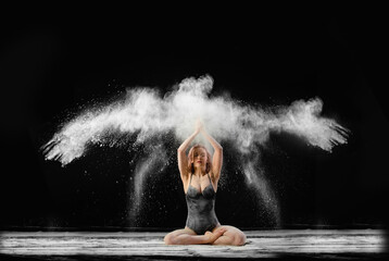 Young beautiful woman with spread flour on the air on a black background