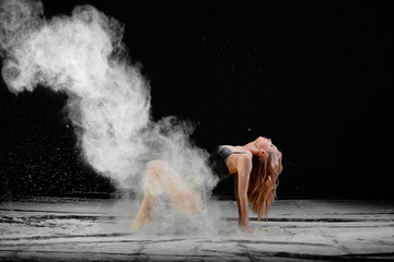 Plakat Young beautiful woman with spread flour on the air on a black background
