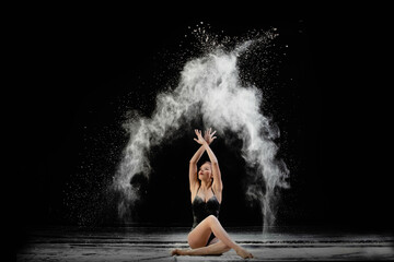 Young beautiful woman with spread flour on the air on a black background