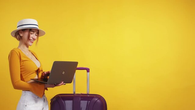 Choosing tour. Inspired woman. Online tickets. Pretty smiling lady in summer look searching on laptop posing with suitcase on yellow background copy space.