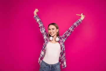 Portrait of a young woman with headphones and a phone on a pink background