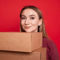 A young woman holds cardboard boxes on a red background.Moving to another apartment