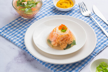 Portioned fish aspic of shrimp, salmon and boiled quail eggs decorated with red caviar and green onions on a white plate on a light background. Recipes fish and seafood.