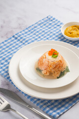 Portioned fish aspic of shrimp, salmon and boiled quail eggs decorated with red caviar and green onions on a white plate on a light background. Recipes fish and seafood.
