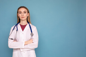 Portrait of a young woman doctor in a white coat and with a stethoscope on a blue background. Copy space. Difficult work of a doctor