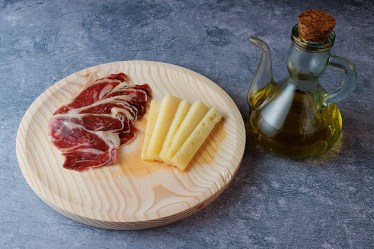 Rustic wooden plate with Serrano Ham and Manchego Cheese accompanied by olive oil