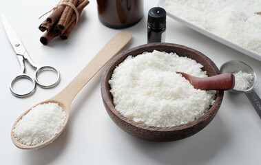 ingredients for candle making , soy wax flakes, candles, cinnamon wicks and wooden spoons on light marble background