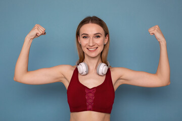 Portrait of an athlete after training. Young woman shows biceps on blue background