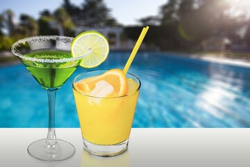 Refreshing tasty alcohol cocktail on swimming pool background