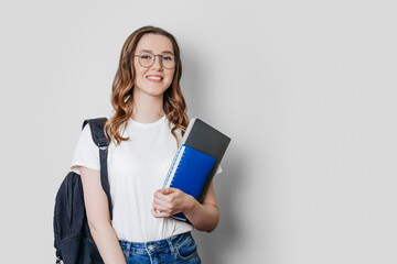 student girl with backpack smiles and holds a notebook, copybook, folder in the hands isolated on dark white background