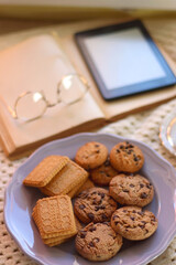 Plate of cookies, cup of tea, fresh blueberries, dry oranges, stack of books, reading glasses and tablet on the table. Hygge at home. Selective focus.