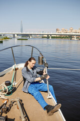 Vertical full length portrait of long haired sailor cleaning boat with care, scene lit by sunlight