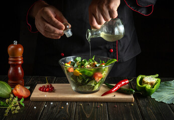 Professional chef adds fragrant oil to the vegetable salad. Vegetarian food by hands of the cook in the kitchen.