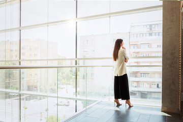 Full length of thinking businesswoman looking the city through window