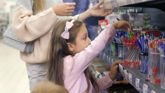 Young beautiful girl walks with her little daughter and son looking at the goods in the office department in a large supermarket.Mom chooses pens and pencils for children.Preparation for kindergarten