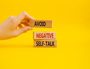 Avoid negative self-talk symbol. Concept words Avoid negative self-talk on wooden blocks. Businessman hand. Beautiful yellow background. Business and Avoid negative self-talk concept. Copy space.