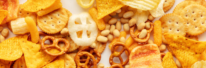 Salty snacks panorama. Party food on white banner. Potato and tortilla chips, crackers and other appetizers, overhead flat lay panoramic shot