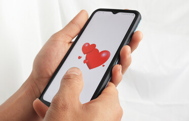 Male hand holding mobile phone with valentine red heart on screen smart phone
