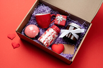 Seasonal gift box for valentine day with candle, red cup and heart shape sweets on red background