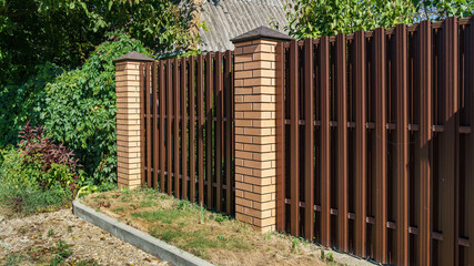 Brown metal fence with brick posts. Metal fencing of private property in the countryside. Security...