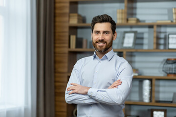 Portrait of successful businessman in office, man in shirt smiling and looking at camera, mature boss with beard with shaggy hands standing at workplace inside building.