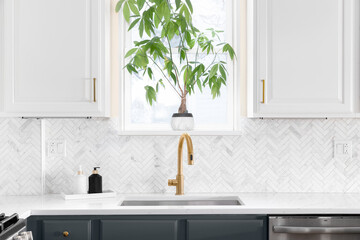 Sink detail shot in a luxury kitchen with herringbone backsplash tiles. white marble countertop,...