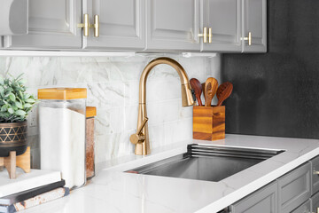 A kitchen sink detail shot with grey cabinets, a white marble countertop and backsplash, and...