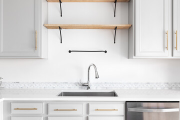 A modern farmhouse kitchen detail shot with grey cabinets, marble countertop and tiled backsplash, gold hardware, and wooden shelves.	
