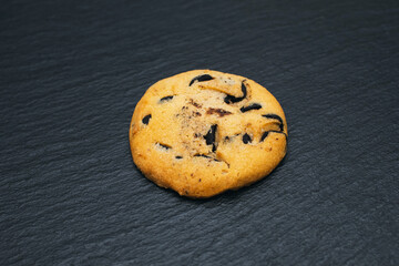 One chocolate chip cookie on a black background. Homemade chocolate chip cookies in the center of the image. Delicious pastries and a quick snack. Sweet dessert in the form of cookies with chocolate