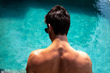 muscular man with his back to the camera looking into a blue pool, person in the pool