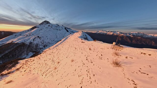 Aerial view snow mountain ridge road at beautiful golden sunset sunrise. FPV sports drone summit ski resort infrastructure ropeway industrial construction dynamic shot picturesque winter cliff valley