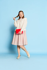 Portrait of funny beautiful girl in vintage style outfit posing over blue background. Retro fashion, business, education and emotions