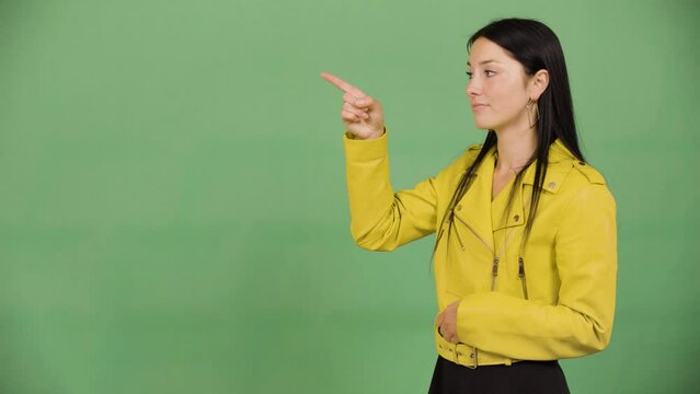 A young beautiful Caucasian woman points at bullet-point text - green screen studio