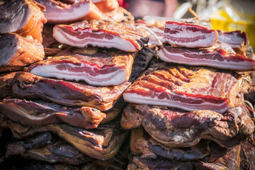 An outdoor stall with pieces of bacon and dried meat being sold
