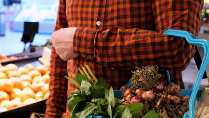 Man picks up an onion from shelf and puts it in shopping basket at grocery store. Buying vegetables at local farmers market. Eating lots onions and vegetables. Buying fresh onions and herbs at market