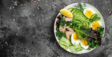 Healthy Food Bowl with Tuna Fish, avocado, egg, cucumber and fresh salad. vegetarian buddha bowl on a dark background. Long banner format. top view
