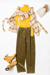 Female winter or autumn stylish clothing set. Plaid checkered shirt, yellow sweater and leather boots, green corduroy trousers, hat with pompom. Trendy fashionable casual clothes. Fashion concept