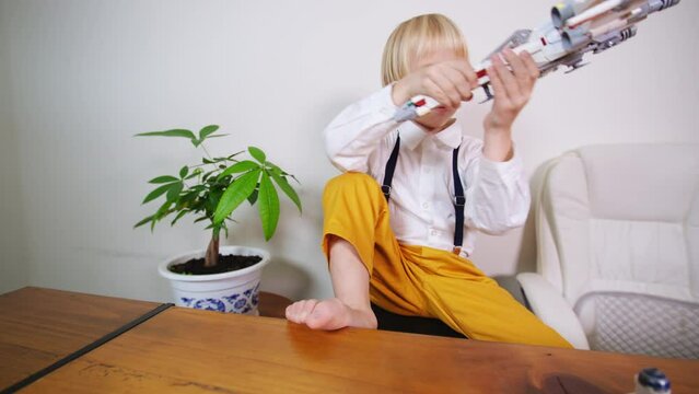 Zooming out view of a blonde caucasian boy playing with Star Wars spaceship from constructor at home. It is a vessel designed for interstellar travel, specifically between star systems