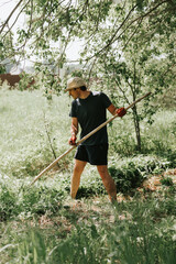 mowing the grass traditional old-fashioned way with the hand scythe on the household village farm. young mature farmer man mowing the grown weed green grass of a farmland with a scythe