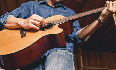Obraz premium Asian male musician hipster playing acoustic guitar or practicing guitar for leisure or hobby hobby ideas for relaxing holiday at home.