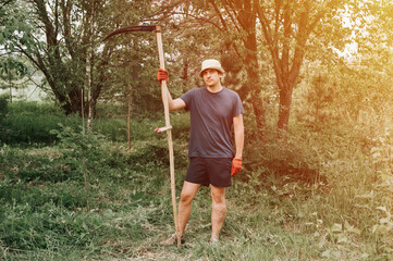 mowing the grass traditional old-fashioned way with the hand scythe on the household village farm. young mature farmer man mowing the grown weed green grass of a farmland with a scythe. flare