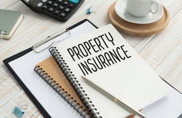 Property Insurance text on paper clipboard with magnifier and keyboard on a wooden background