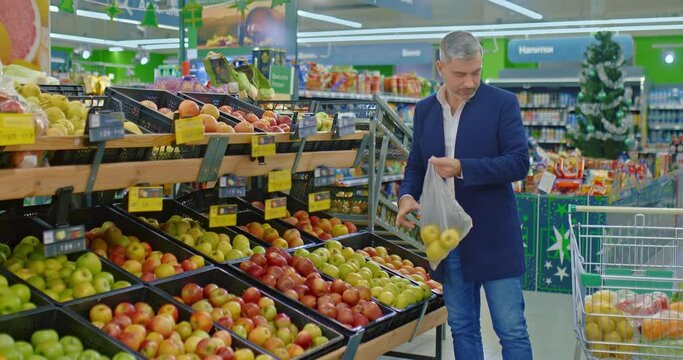 adult man shopping in supermarket before Christmas, buying yellow apples, 4K, Prores
