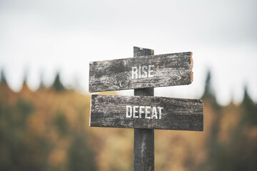 vintage and rustic wooden signpost with the weathered text quote rise defeat, outdoors in nature. blurred out forest fall colors in the background.