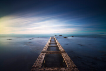 Wooden pier remains in a blue sea. Long Exposure.