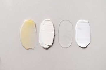 Yellow gel, scrub, transparent facial serum and white cream swatches. Beauty routine four steps smears. Different skin care products texture. Cosmetic smudge on light grey background.