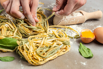 Female hands holding Fresh homemade green and yellow pasta tagliatelle. Raw homemade spinach pasta