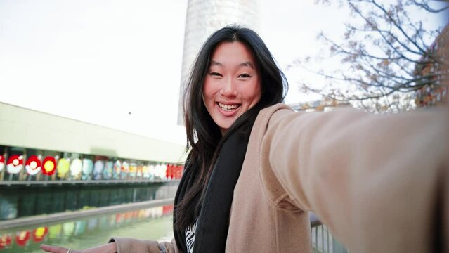 Happy asian young lady taking a selfie photo with an smartphone. Self portrait of chinese smiling woman doing the peace sign after shopping outdoors. High quality 4k footage