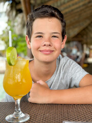 Young boy is enjoying on the beautiful tropical beach at summer with a fresh drink.